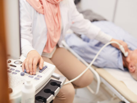 Closeup of unrecognizable female doctor using ultrasound machine while examining senior patient in clinic